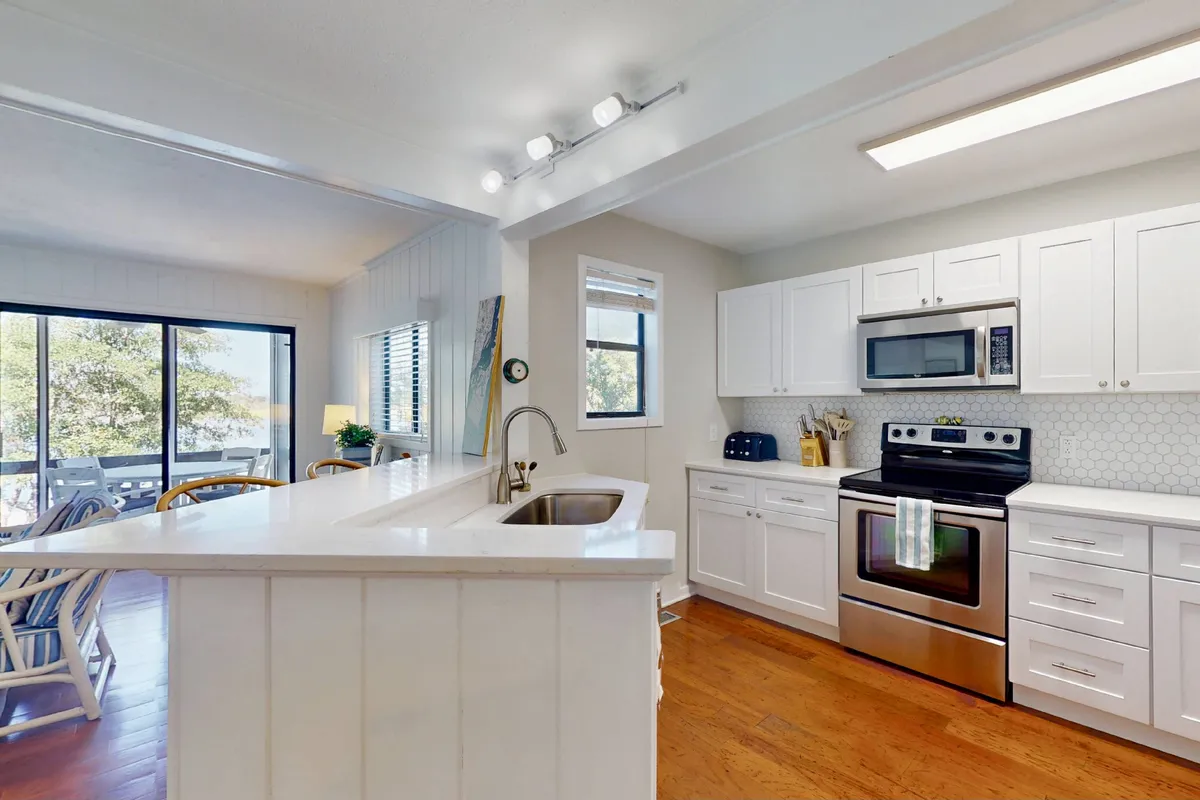 A bright, remodeled kitchen with a central island, stainless steel appliances, and a window looking out to lush scenery. The space is open and inviting, emphasizing modern updates and ample room for cooking and gathering.