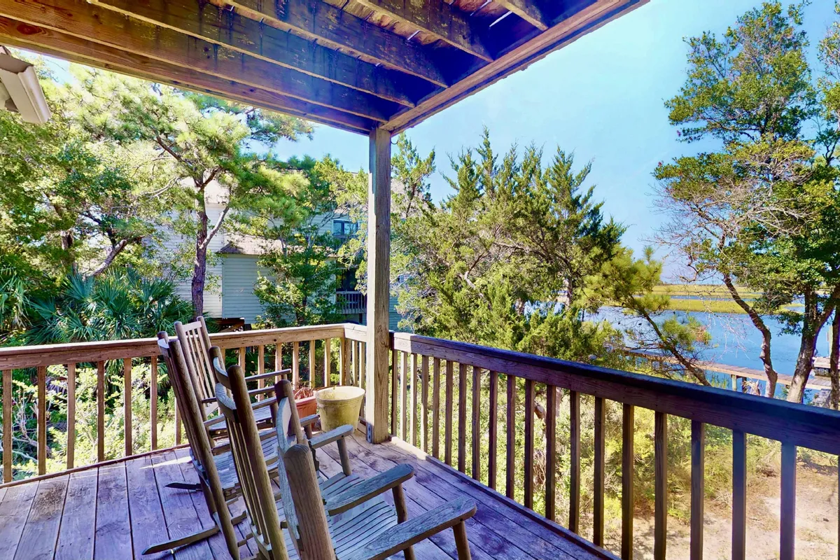 An inviting exterior with classic rocking chairs on a porch, looking out over serene water and surrounded by trees. The setting is tranquil, ideal for sipping a drink, reading, or simply watching the sunset.