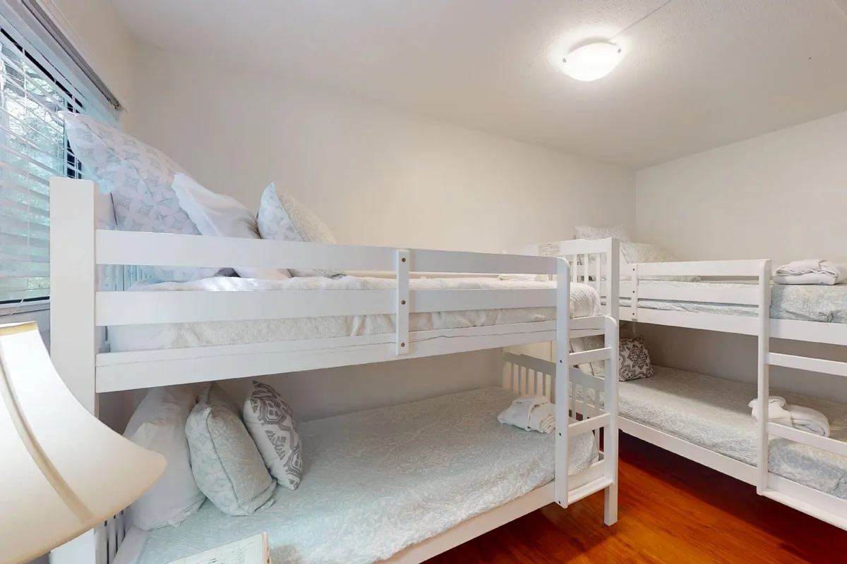 A cheerful bunk room with four twin bunks, each adorned with colorful decorative pillows and a cozy lamp, creating a welcoming space for children or friends. The room exudes a sense of playfulness and comfort, ideal for building memories.