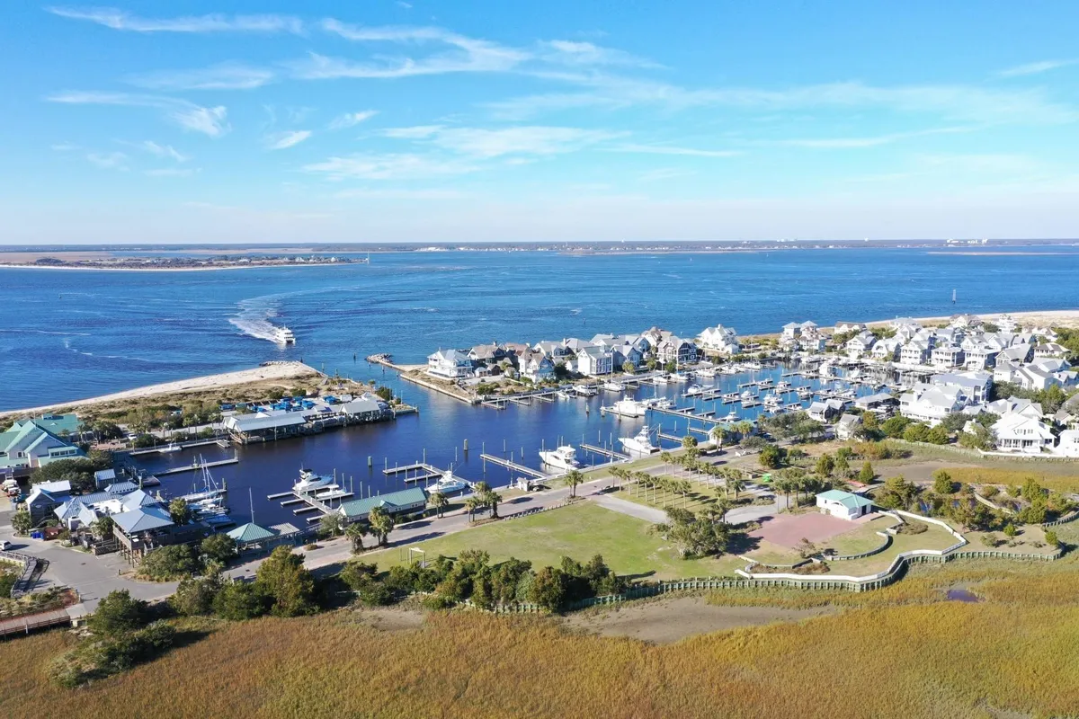 A vibrant marina scene features boats docked along calm waters, with charming houses and a waterway in the background. The area is lively yet relaxed, ideal for strolling, boating, or simply soaking in the waterfront atmosphere.