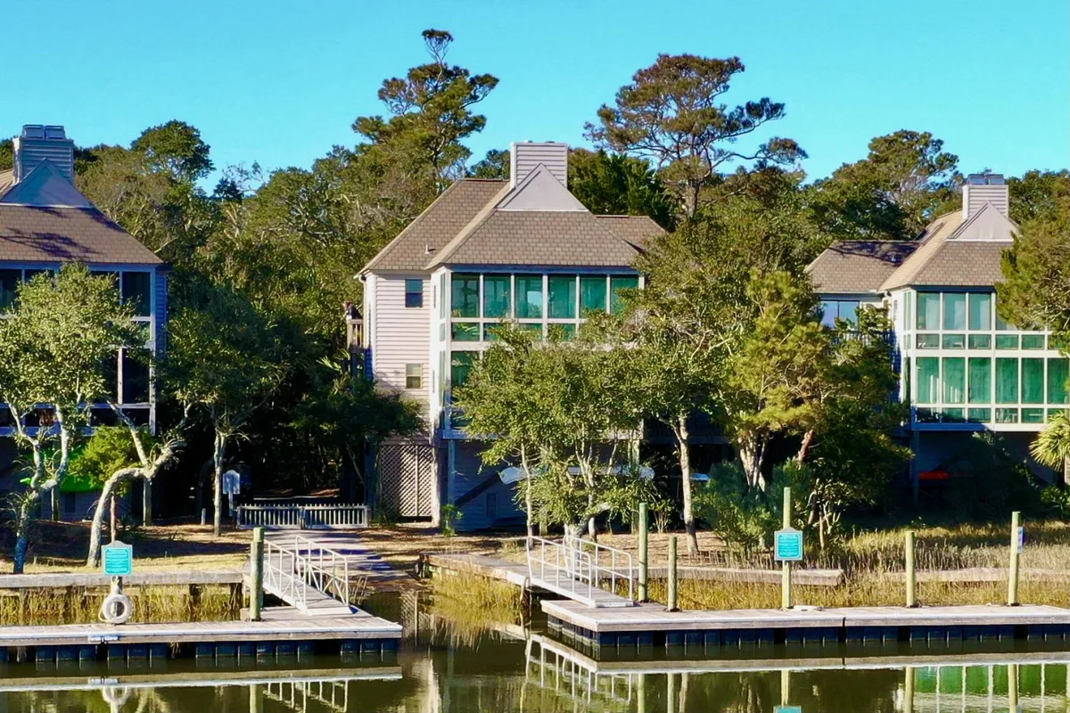 A peaceful exterior shot showing two large houses with expansive windows, a dock leading to the water, and lush natural surroundings. This image highlights easy access to water activities and the integration of homes with the natural environment.