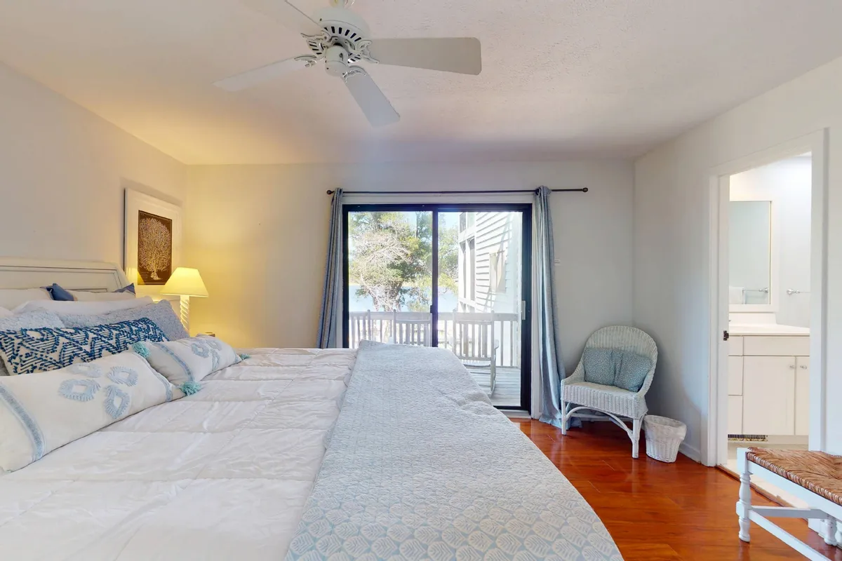 A serene and spacious primary bedroom featuring a large king bed with decorative pillows, a comfortable reading chair in the corner, and a sliding glass door that opens directly onto a private porch. The room is filled with natural light and offers a peaceful retreat after a day of adventure.